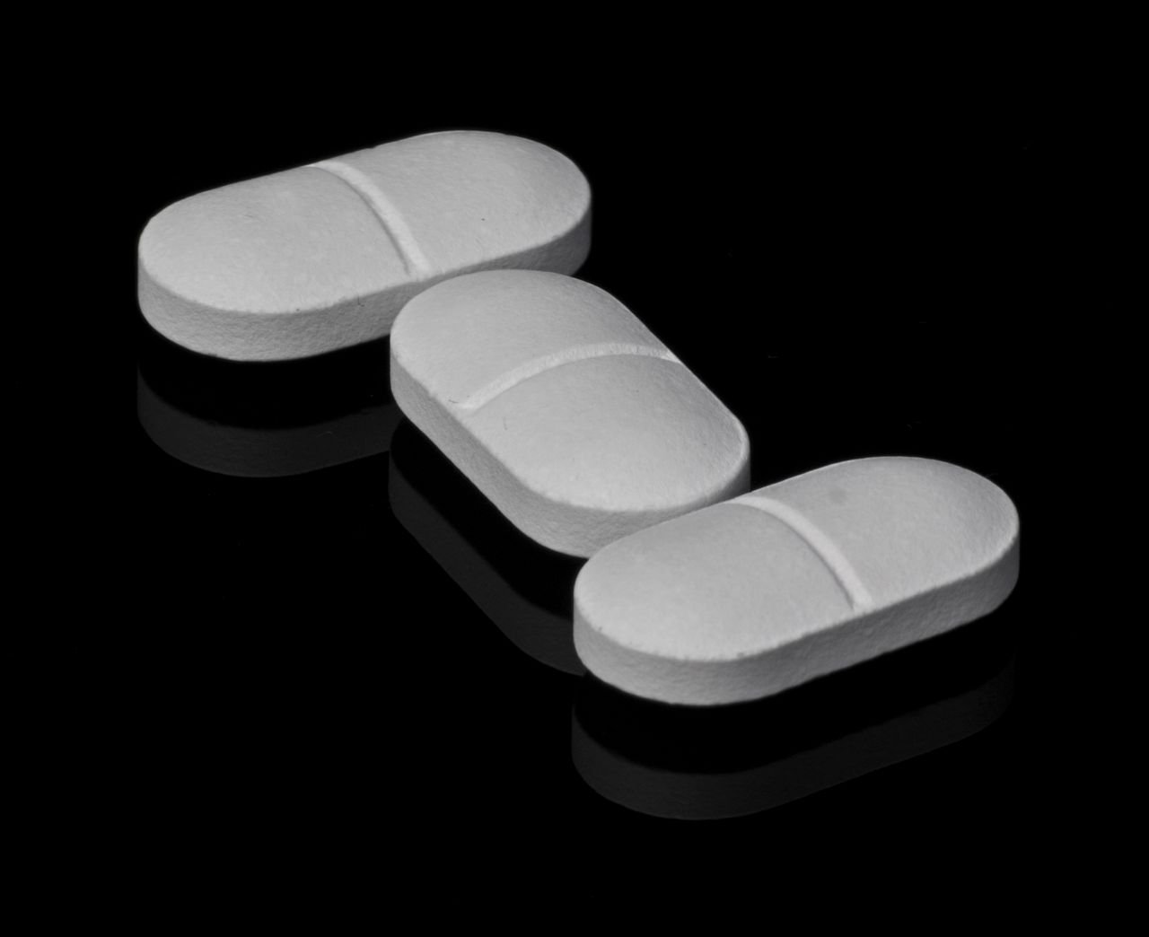 About Three white tablets placed on a black reflective surface, highlighting pharmaceutical theme.